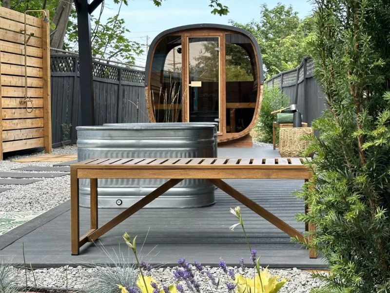 Garden sauna cabin with cold plunge tub, deck seating, and lush greenery.