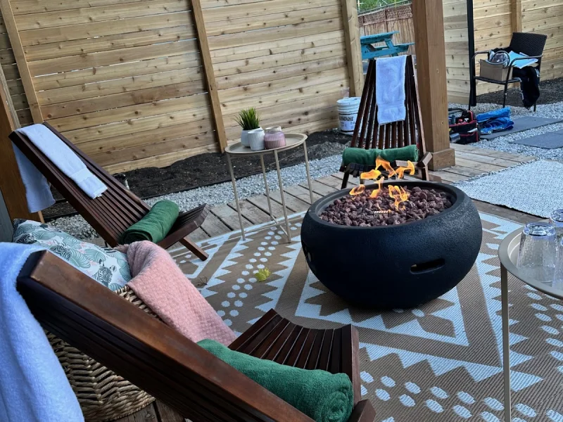 Covered outdoor fire pit lounge with Adirondack chairs, towels, and patterned rug.