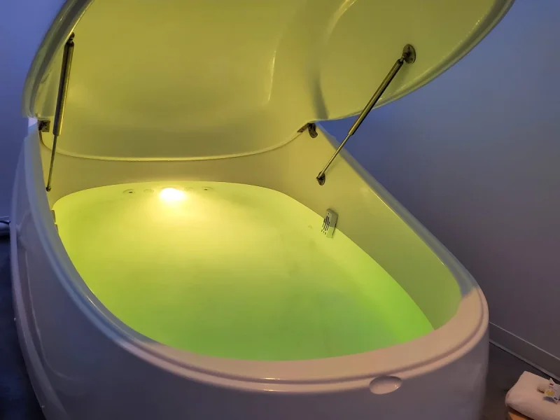 Luxury float therapy pod with luminous lime-green water and ambient blue-purple lighting