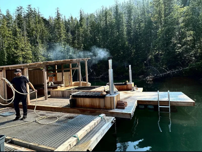 Guest soaking in steaming hot tub with forest and lake views at wellness retreat