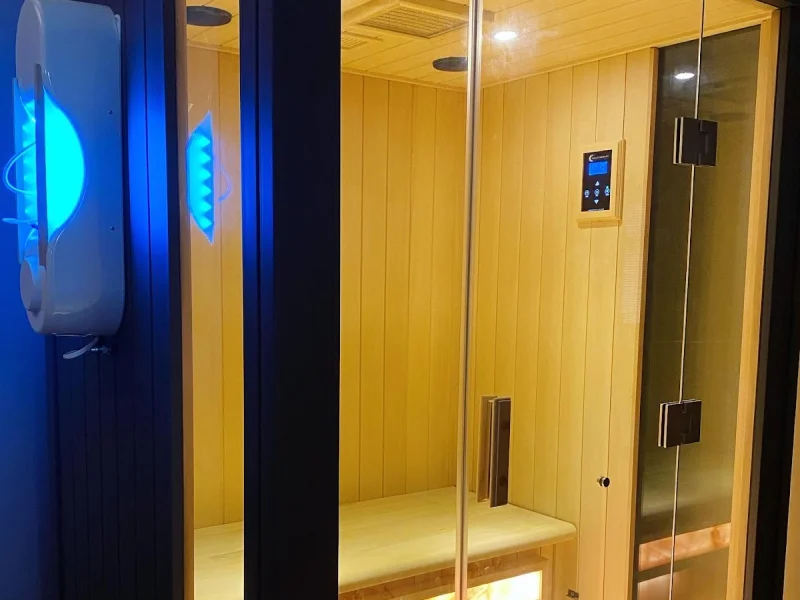 Light wood infrared sauna with glass partition and blue-lit adjacent wellness pod
