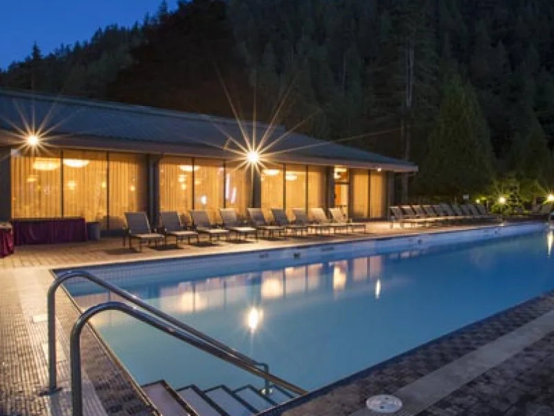 Outdoor resort pool at night with mountains and lounge chairs