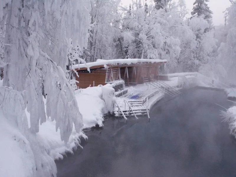 Snow-covered hot springs in winter with steaming water and frozen trees