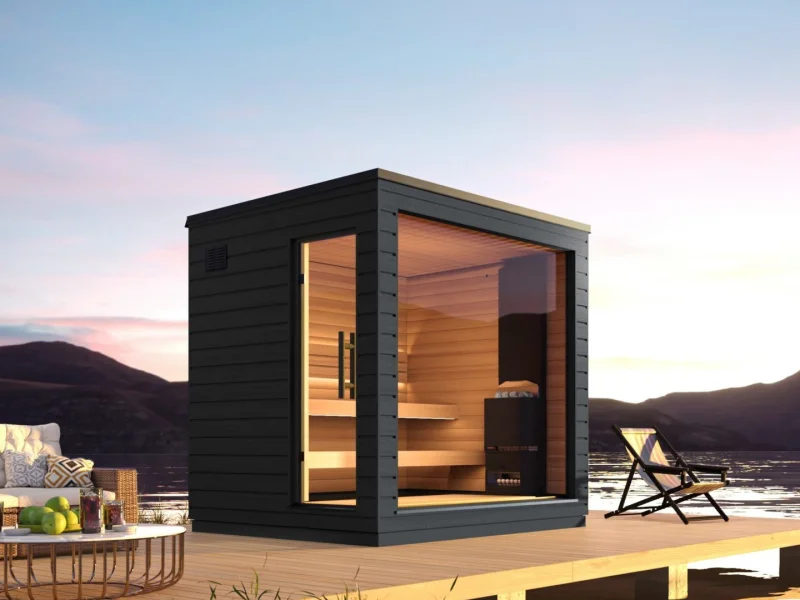 Modern compact sauna cabin on a lakeside deck at sunset