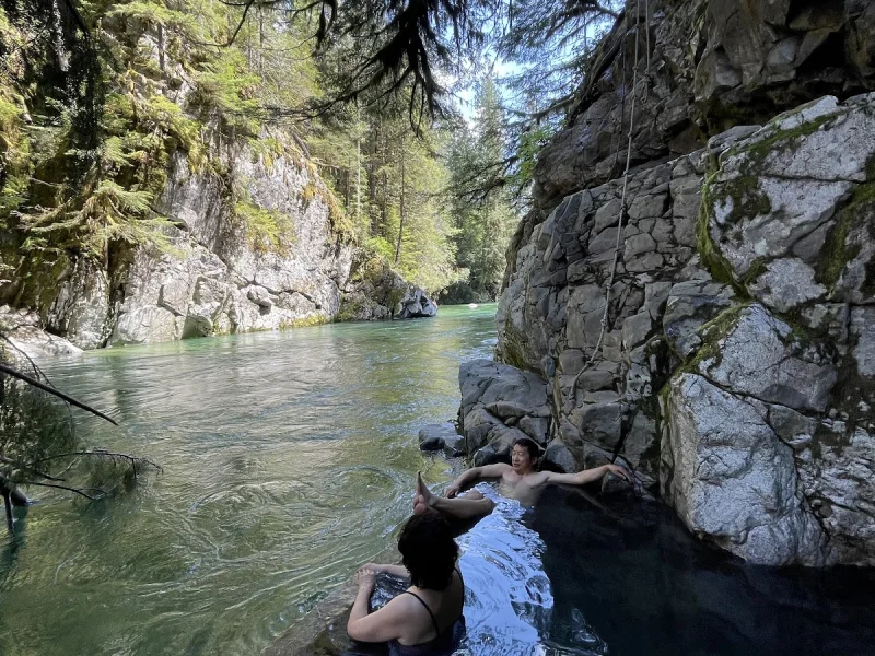 Secluded cliffside hot spring with guests soaking in clear wilderness water