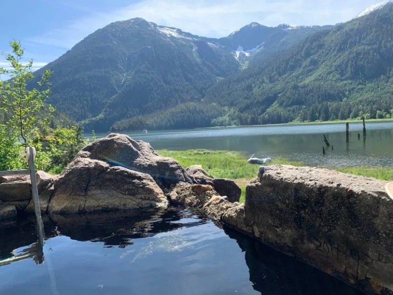 Scenic outdoor hot spring with mountain and lake views in a remote coastal valley