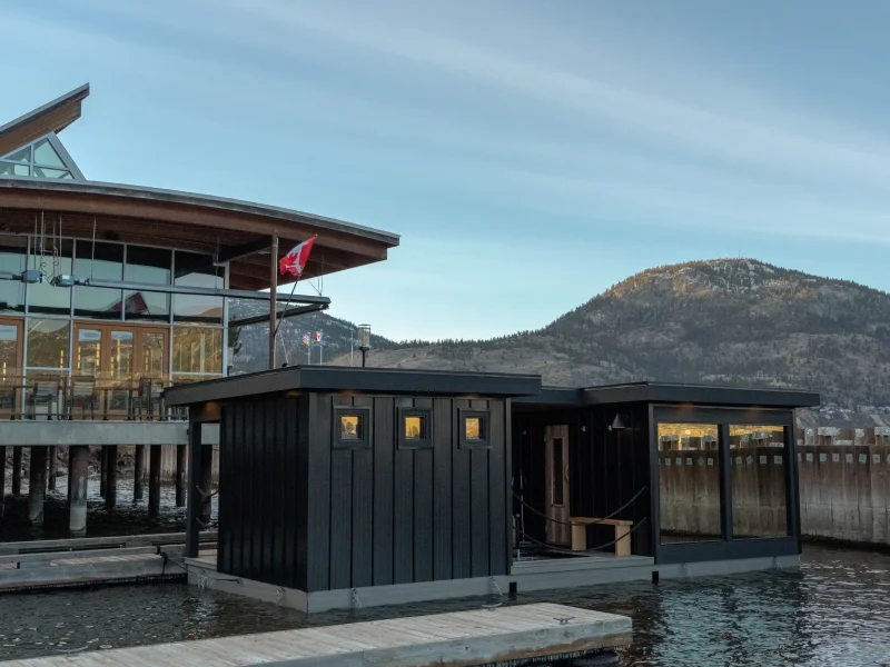 Floating sauna building beside the water with mountains and lakeside views