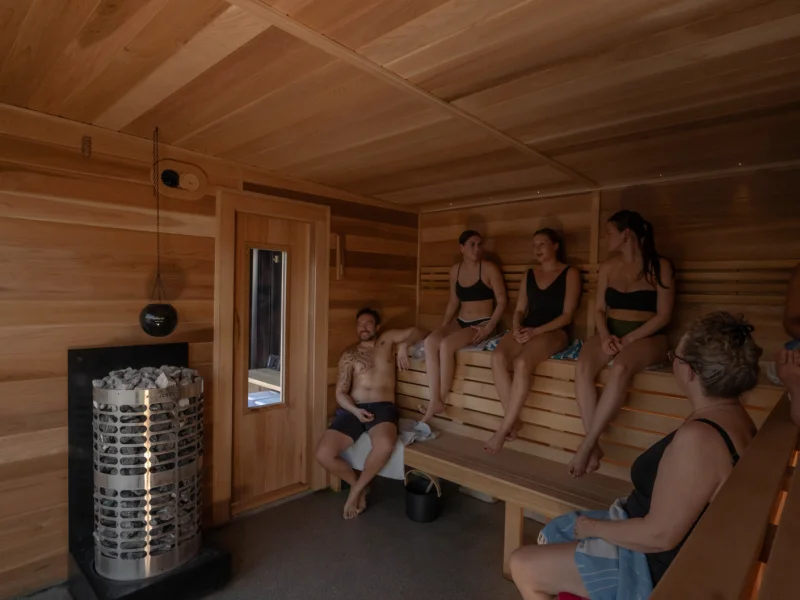 Wood-lined sauna interior with guests seated around the heater