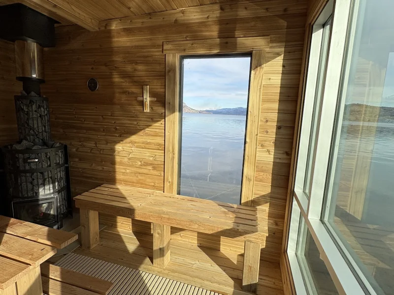 Wood-lined floating sauna interior with lake view and heater