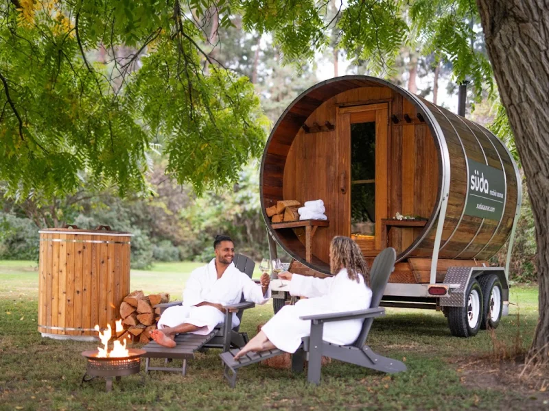 Outdoor barrel sauna with hot tub, fire pit, and guests in robes under trees