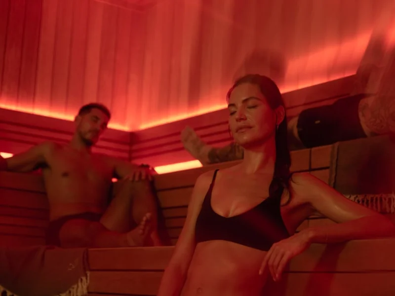 Guests relaxing in a red-lit sauna with warm wood benches