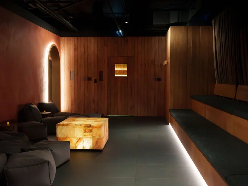 Relaxation lounge with dark seating, wood walls, and glowing accent cube