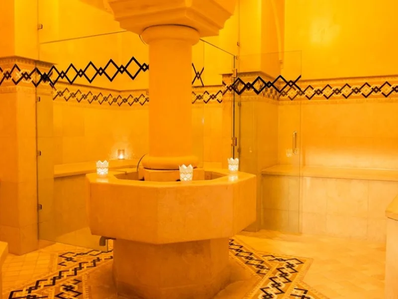 Golden-lit hammam thermal chamber with ornate ceiling, heated platform, and ceremonial candles